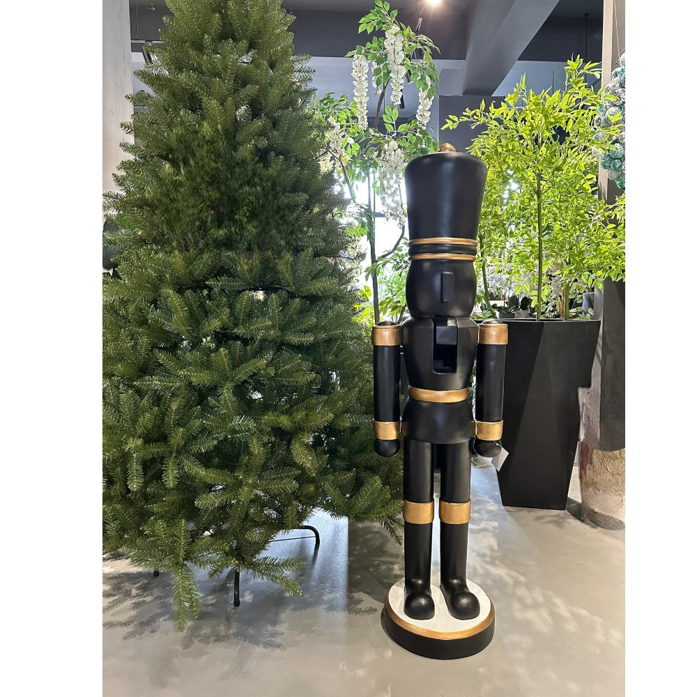 Black and gold resin Christmas nutcracker displayed beside a Christmas tree