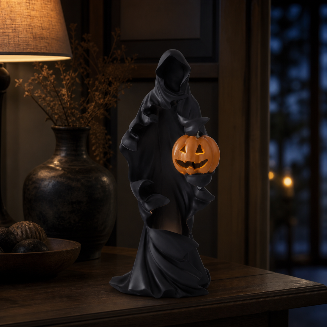 Black draped LED ghost holding one glowing jack-o'-lantern on a dark wood console