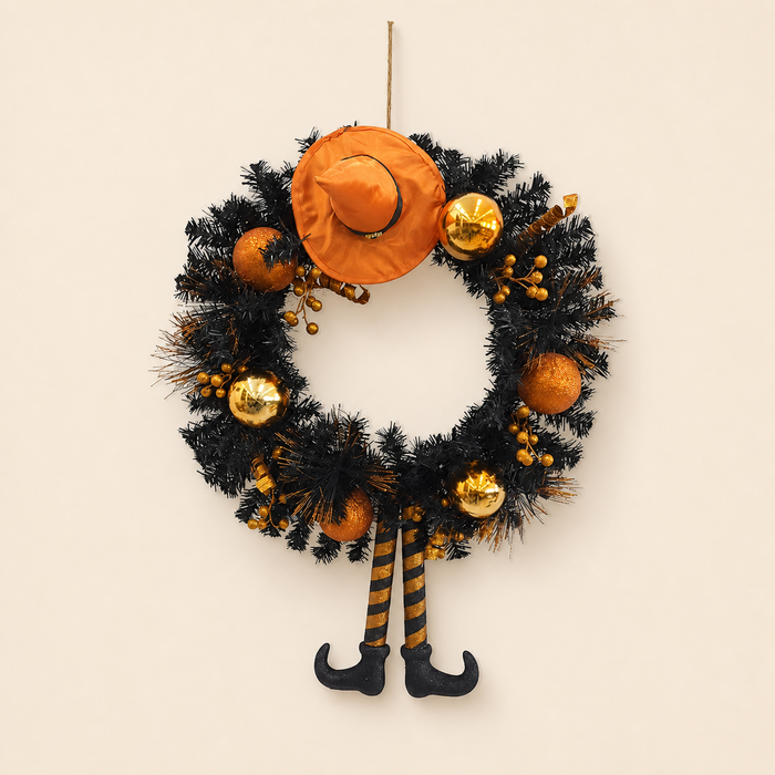 Black Halloween wreath with orange witch hat and striped legs on a neutral background