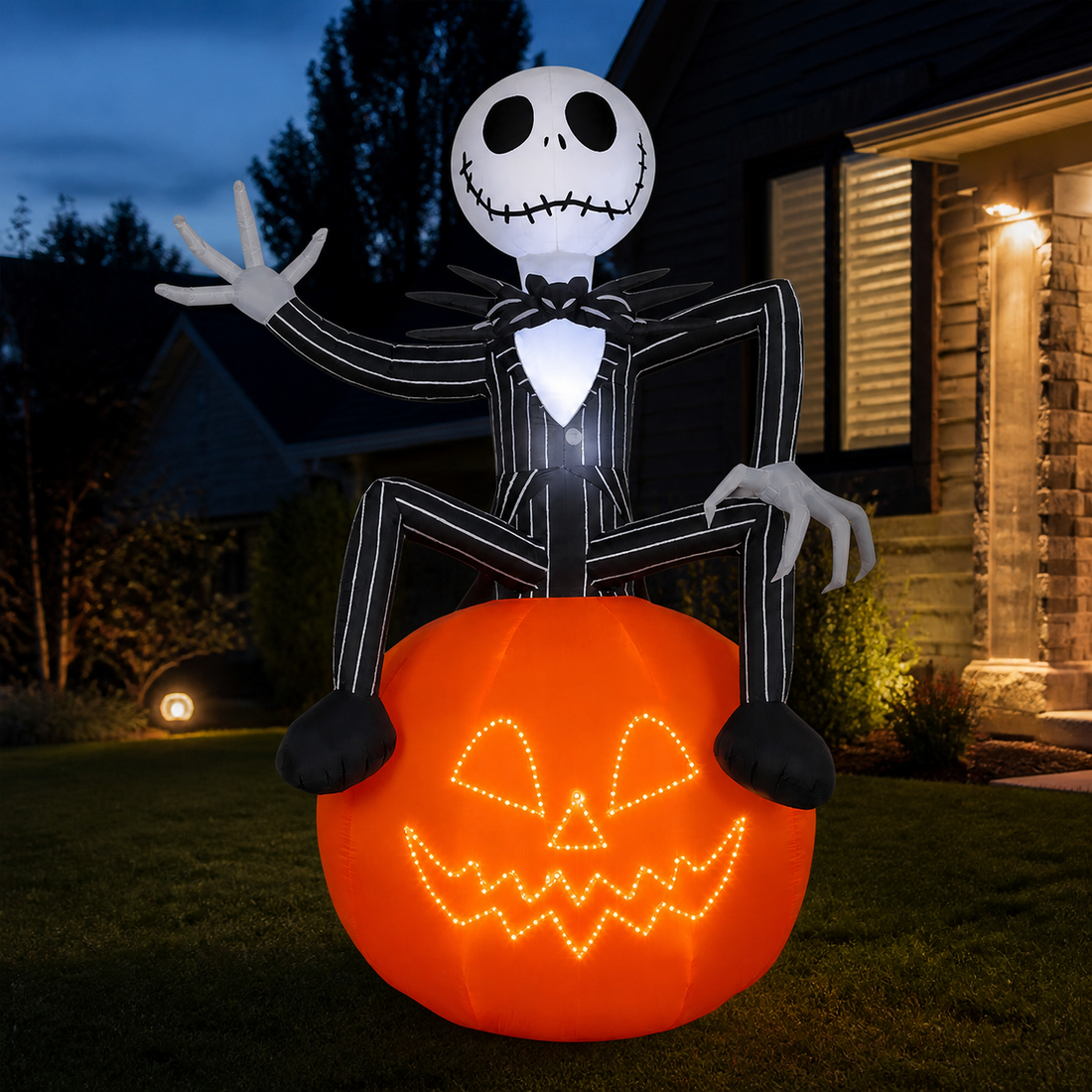 Giant Jack Skellington inflatable seated on an illuminated pumpkin in a Halloween yard at dusk