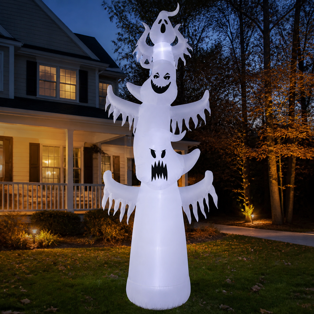 Three stacked light-up white ghost inflatables displayed in a front yard at dusk